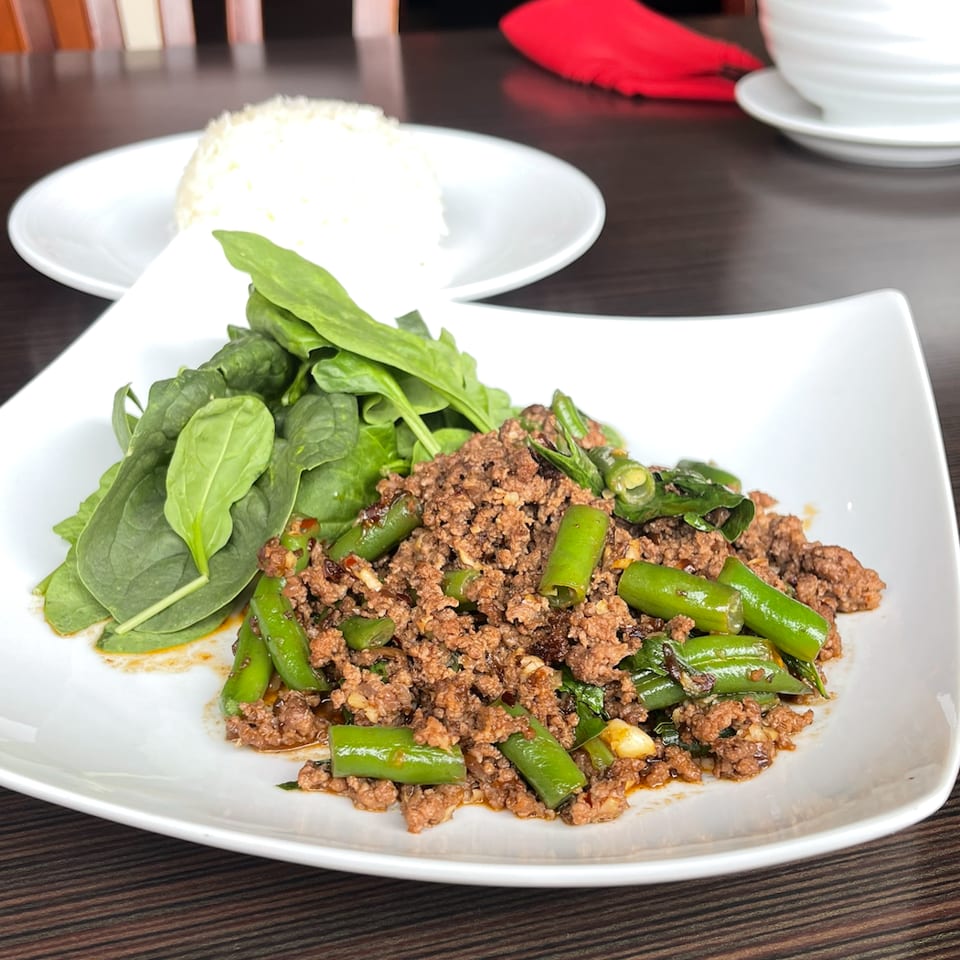 Spicy minced meat stir-fried with green chilies and leafy greens, served with white rice on a square plate.