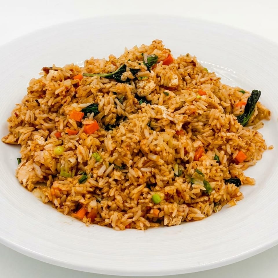 Plate of golden fried rice with diced carrots, green onions, leafy vegetables, and pieces of chicken.